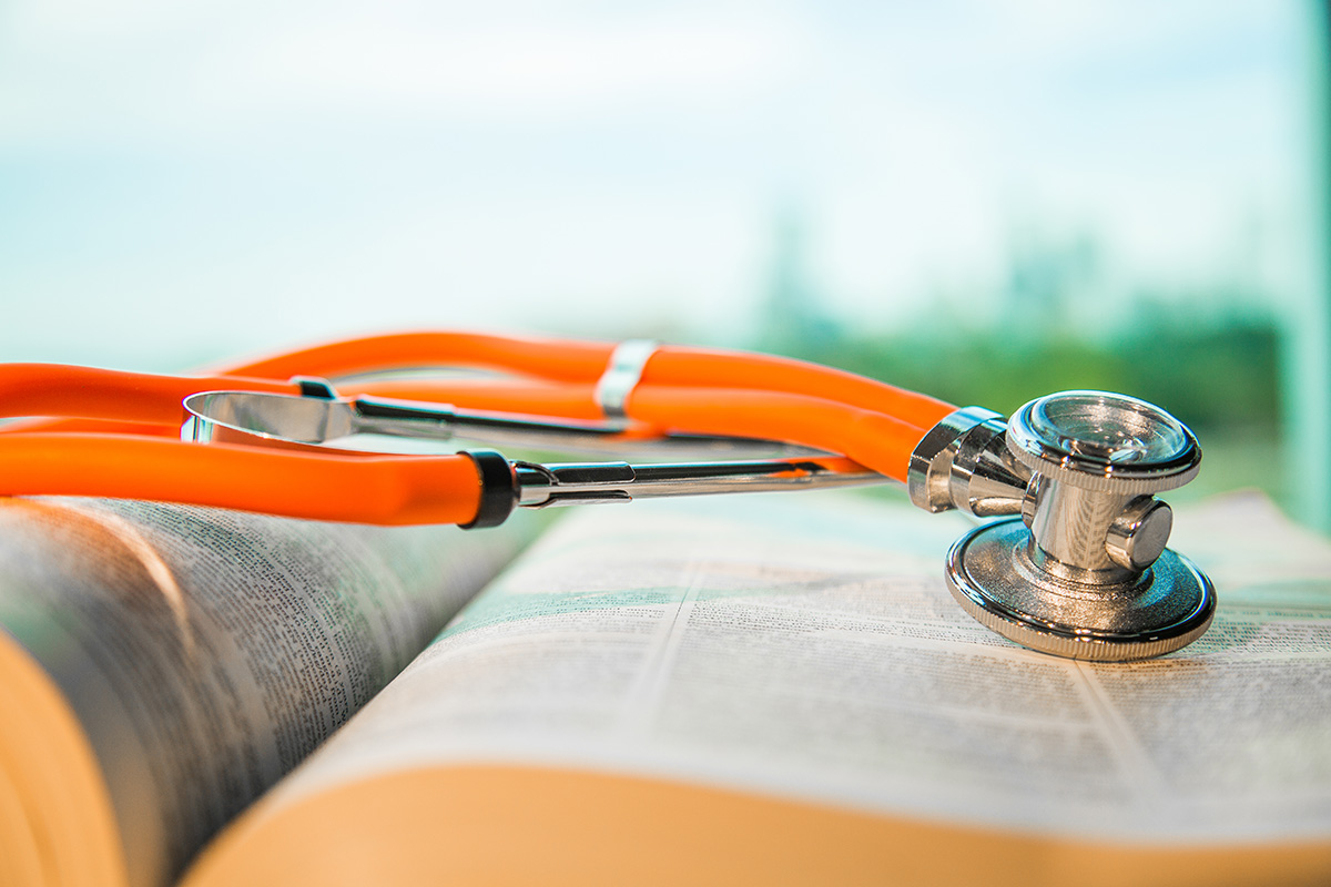 Orange stethoscope laid on top of a textbook.