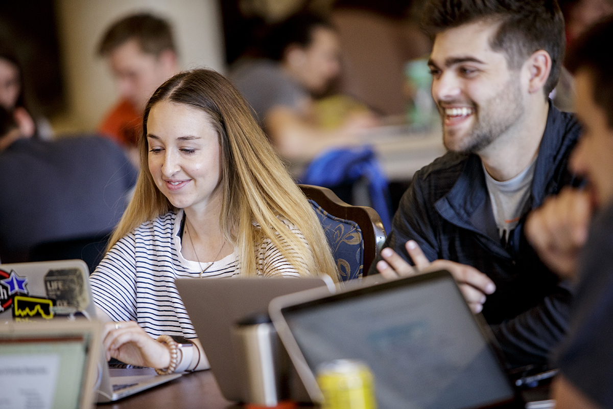 Students smiling together while working at laptops.