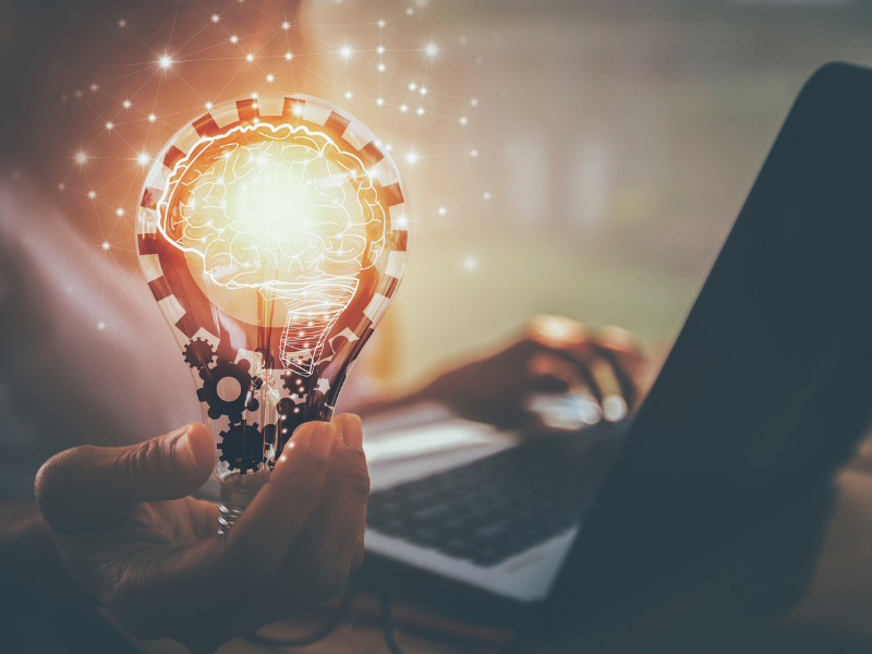 A lightbulb held up with a laptop in the background.