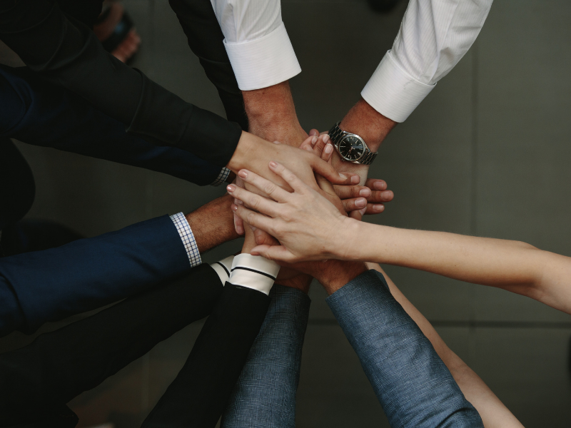 A group of people in a circle, with their hands stacked in the middle. A group of people in a circle, with their hands stacked in the middle.